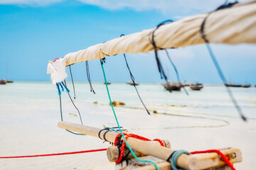 Near a tropical island, a traditional Zanzibar fishing boat lies in clear water close to the beach,...