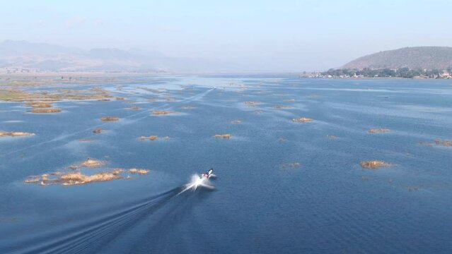 Single traditional long boat on full speed cruising over Moebyel Lake in Myanmar. Panoramic drone lifting shot