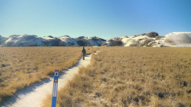 Adult black male walking hiking away on trail white sands national park sand dunes landscape with mountains in New Mexico, USA