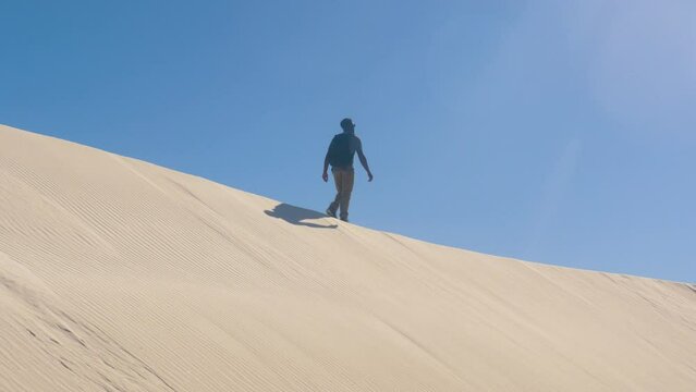 Adult black male walking hiking on sunny white sands national park sand dunes landscape with mountains in New Mexico, USA