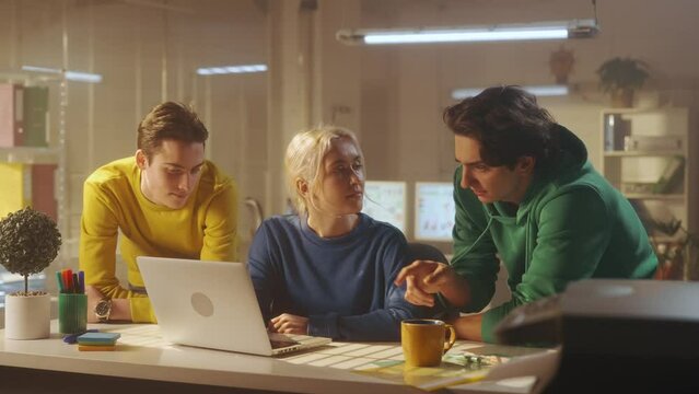 A young woman presents a new project on a laptop to their male colleagues managers. The leader shows the work plan to his team while sitting at the table in a modern office. Brainstorm. Team building.