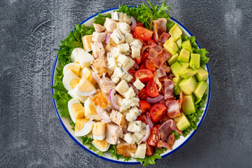 Tradition Cobb salad with fried chicken, avocado, fresh tomatoes, eggs, bacon and cheese on a plate on a dark background. Top view, copy space, selective focus
