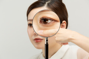 女性の下瞼をルーペで拡大している。 - obrazy, fototapety, plakaty