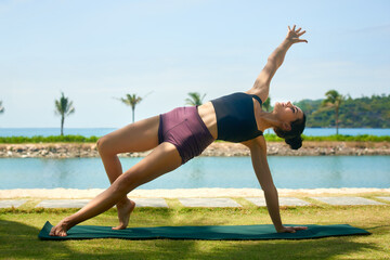 Woman wearing active wear doing yoga practice on background of beach. Meditation in sunny day, No stress, inner balance concept.