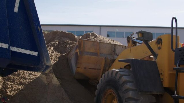 Large yellow construction machine at a cement plant, loading the front trailer with sand to be transported to the construction companies. The process of loading sand, gravel, cement into trucks.