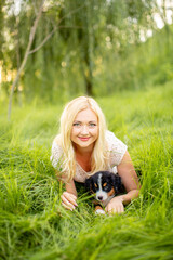 A beautiful girl with a dog sits in the park on the grass. Love to the animals. Home pet on a walk. Animal protection. Bernese mountain dog puppy.