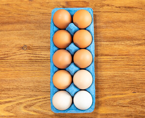 A dozen fresh chicken eggs in a blue cardboard tray on an orange-brown wooden textured background