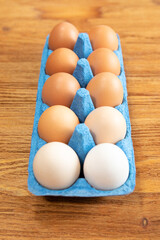 Close-up of a dozen fresh chicken eggs in a blue cardboard tray on an orange-brown wooden textured background