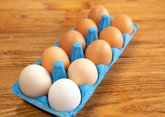 Close-up of a dozen fresh chicken eggs in a blue cardboard tray on an orange-brown wooden textured background