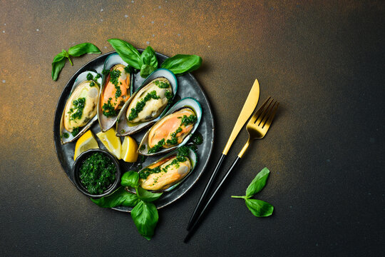 Close up of delicious steamed mussels with basil and garlic. On a black stone plate. Seafood.
