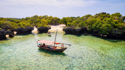 Obraz na płótnie Canvas From above, the stunning landscape of Zanzibar's tropical coast comes into focus, with fishing boats lined up on the sandy beach at sunrise. The view from the top reveals a clear blue sea, green palm 