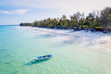 The natural beauty of Zanzibar's tropical coast is on full display in this aerial view, with fishing boats lining the sandy beach at sunrise. The top-down perspective showcases clear blue waters,