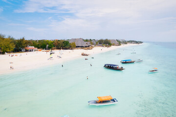 Fototapeta na wymiar From above, the stunning landscape of Zanzibar's tropical coast comes into focus, with fishing boats lined up on the sandy beach at sunrise. The view from the top reveals a clear blue sea, green palm 