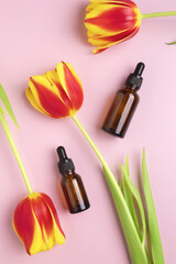 Obraz na płótnie Canvas Cosmetic bottles made of amber glass and tulips on a pink background. The concept of natural cosmetics and minimalistic packaging. The concept of skin care.