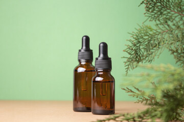 Glass dropper bottles with cosmetic oil, essential or serum on green background with thuja branches. Hyaluronic acid oil, serum with collagen and peptides skin care product.