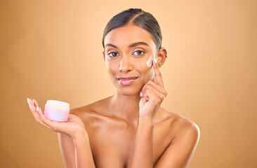 Face, skincare and woman with cream jar in studio isolated on a brown background. Dermatology cosmetics, portrait and happy Indian female apply lotion, creme and moisturizer product for healthy skin.