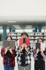 Attractive diverse students in casual style covering face by the book at the library