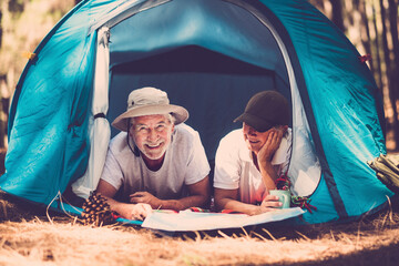 Portrait of senior couple relaxing inside a tent in free camping woods alternative travel vacation...