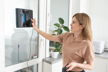 Woman cleaning windows at home with robotic cleaner.