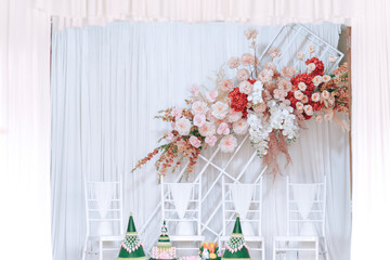 The wedding backdrop features white chairs and is decorated with delicate pink flowers. Thai wedding concept.