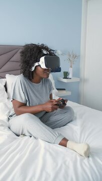 African female gaming enthusiast enjoys virtual reality on bed in the morning.