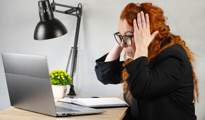 Office worker. Happy girl at the laptop in the office. A businesslike, cheerful woman in an office suit is doing her job.