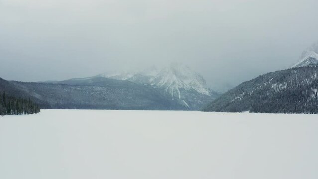 Low aerial over beautiful frozen lake with large foggy mountains behind
