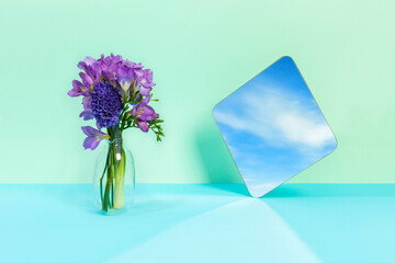 The sky is reflected in the mirror on the colored background, the flower next to it