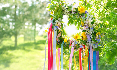Floral wreath with colorful ribbons on tree in garden, green natural background. floral decor,...