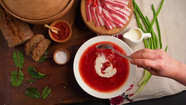 Woman serving hot Ukrainian borscht. Traditional Ukrainian borscht. Bowl of red beet root soup borsch with white cream . Beet Root delicious soup. A plate with chopped lard. Traditional Ukraine food c