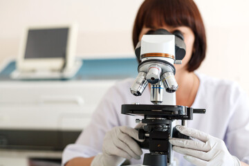 Female lab scientist researcher technician worker in gloves sits next to a microscope in laboratory