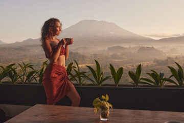 Woman enjoys coffee on yoga retreat at a luxurious resort with stunning views of Agung volcano and...
