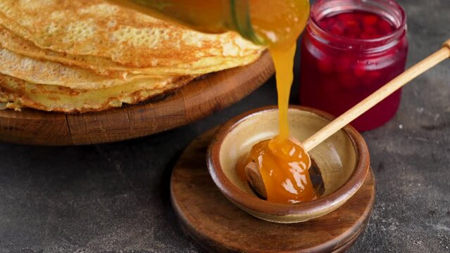 Shrovetide - Pancakes and Honey. Honey spoon. Honey drips from a glass jar into a bowl. Close-up. Healthy organic thick honey dipping from a wooden honey spoon, close up.