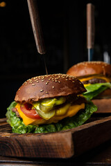 Two burgers on a wooden board with a knife and fork on it