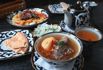 Lunch in ethnic, national, Uzbek style. Uzbek lunch with shurpa, pilaf, green tea in a teapot.