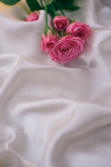 Pink roses on white satin fabric as background. Soft focus.