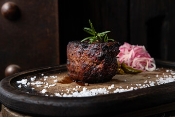 A steak on a wooden board with salt and pepper on it.