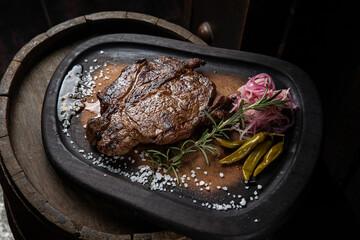 A steak on a wooden board with salt and pepper on it.