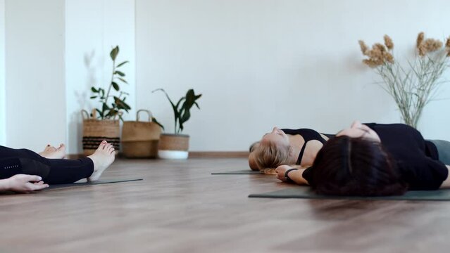 Women in sportswear are lying on floor with mat doing yoga in fitness club, front view. Women group training at yoga classes. Concept of spirit mental and meditation