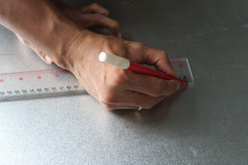 A worker drawing straight line on metal sheet with ruler and marker