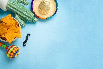 Mexican party concept with cactus, nachos chips, maracas and sombrero hat on blue background. Cinco...
