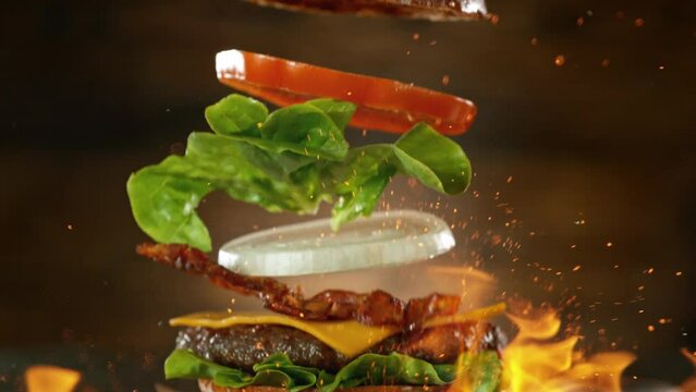 Beef Burger Ingredients Falling and Landing in the Bun with Fire Flames. Camera Move. Super Slow Motion at 1000 fps.