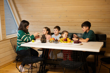 Mother with four children eat fruits in wooden country house on weekend.