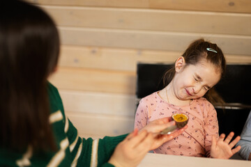 Mother with daughter eat fruits, she gave a passion fruit. Girl grimaced from the sour taste.