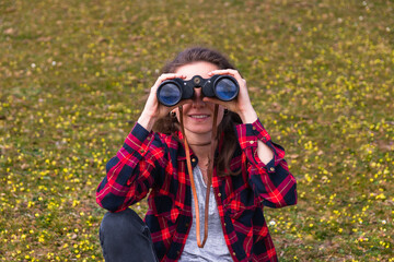 Young woman looking trough binoculars directly to the camera and smiling