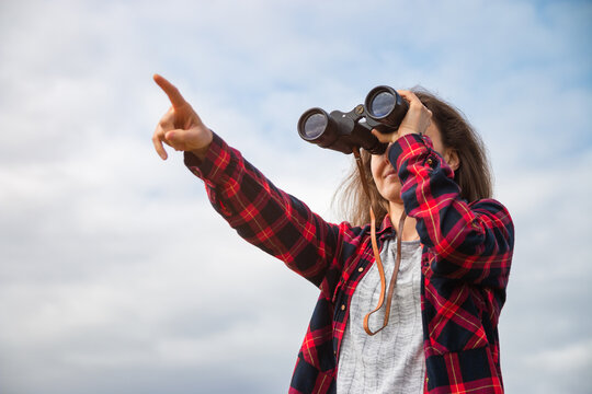 Woman looking trough binoculars on a sunny day with the sky as background and pointing to the sky with her finger - Powered by Adobe