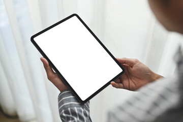 Closeup over shoulder view man holding digital tablet standing in bright office. Blank screen for your advertising text message