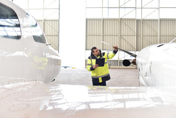 Aircraft mechanic inspects and checks the technology of a jet in a hangar at the airport - 584609366