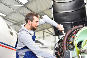 Aircraft mechanic repairs an aircraft engine in an airport hangar - 584609503