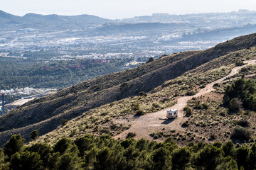 a single camper is parked on a gravel road in the mountains. mountain view, no people, horizontal
